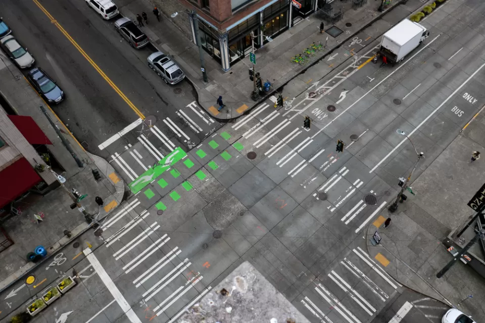 An almost empty intersection in downtown Seattle Washington. An arial shot off of the side of a building that shows the crisscrossing of roads, crosswalks, and bike lanes.
